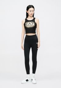 Fekete, rövidített trikó "EA7 Emporio Armani" logóval, magas derekú fekete leggingsszel párosítva. Fehér tornacipő fekete részletekkel.