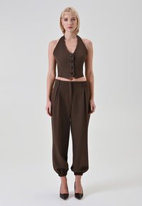 Top corto marrone a righe sottili con collo all'americana e bottoni, abbinato a pantaloni marroni a righe sottili, larghi, con polsini elastici e pieghe.