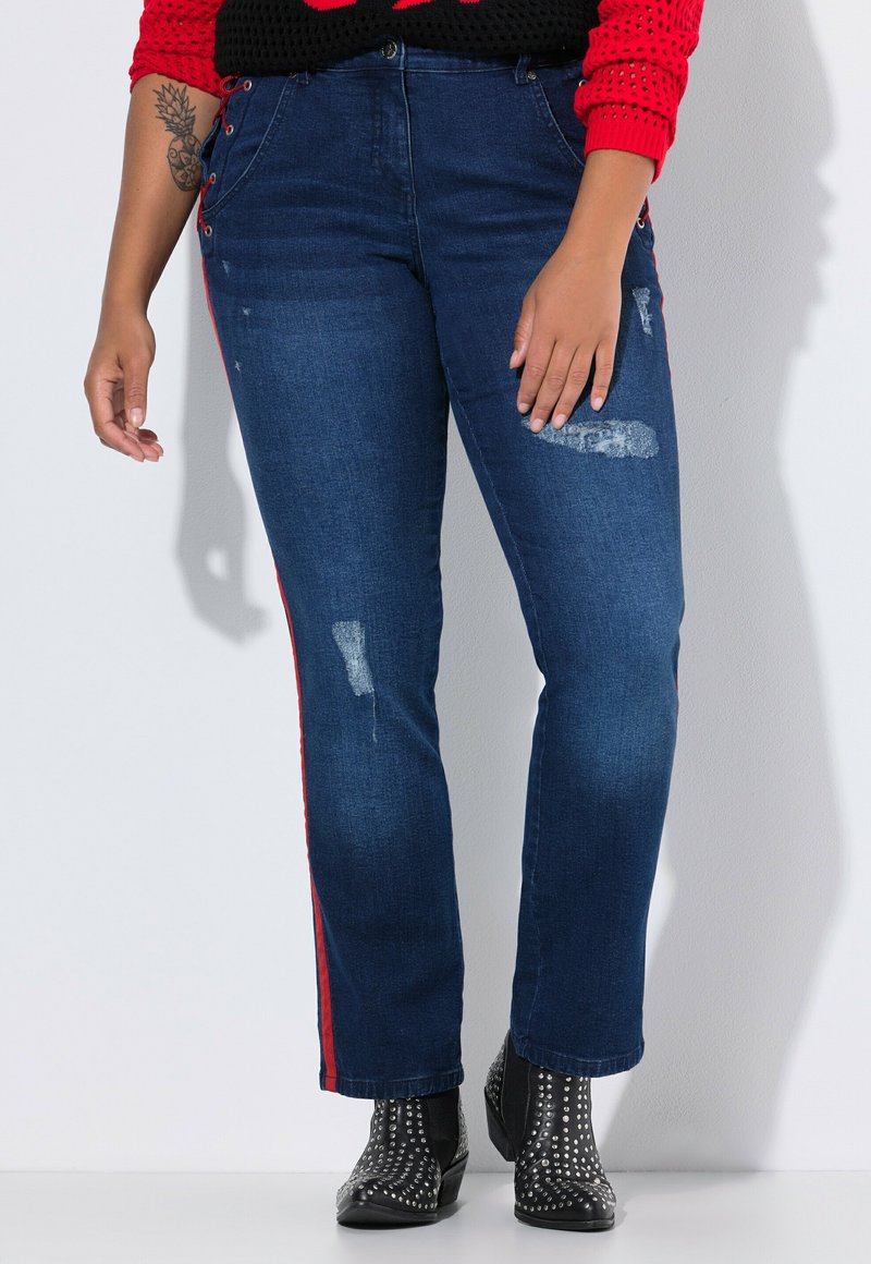 Tummansiniset farkut punaisilla sivuraidoilla, joissa on kulutettuja yksityiskohtia ja suora lahje. Yhdistetty niittikoroilla varustettuihin mustiin nilkkabootseihin.