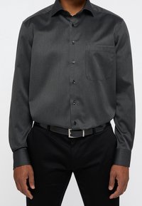 Zwart patroon overhemd met lange mouwen, voorzien van knoopsluiting aan de voorkant, scherpe kraag, borstzak en manchetten, gedragen met een zwarte broek en een riem.