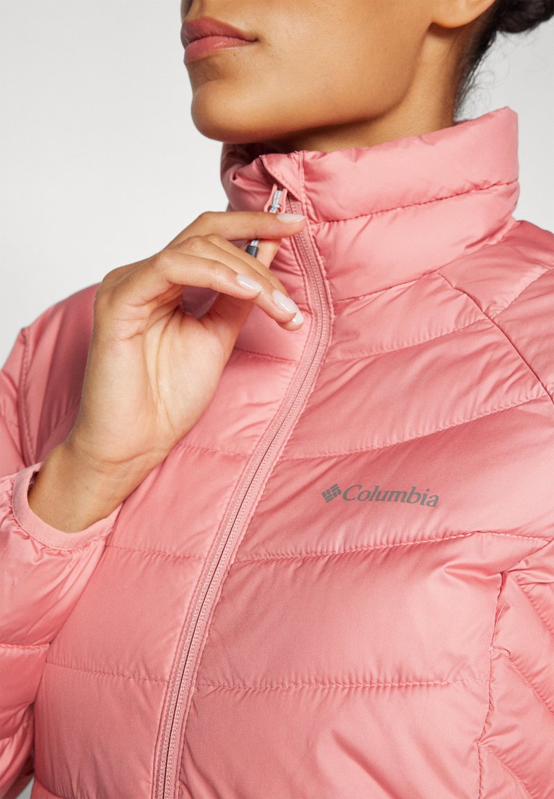 Giacca imbottita rosa con colletto alto e chiusura a zip. Presenta il logo Columbia e bordi a coste sui polsini per una vestibilità sicura.