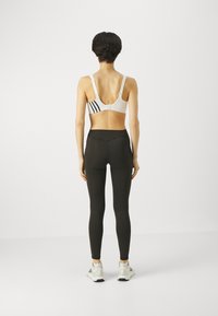 Sostén deportivo blanco con rayas negras, combinado con leggings negros de cintura alta. El conjunto resalta un diseño ajustado adecuado para ropa activa.