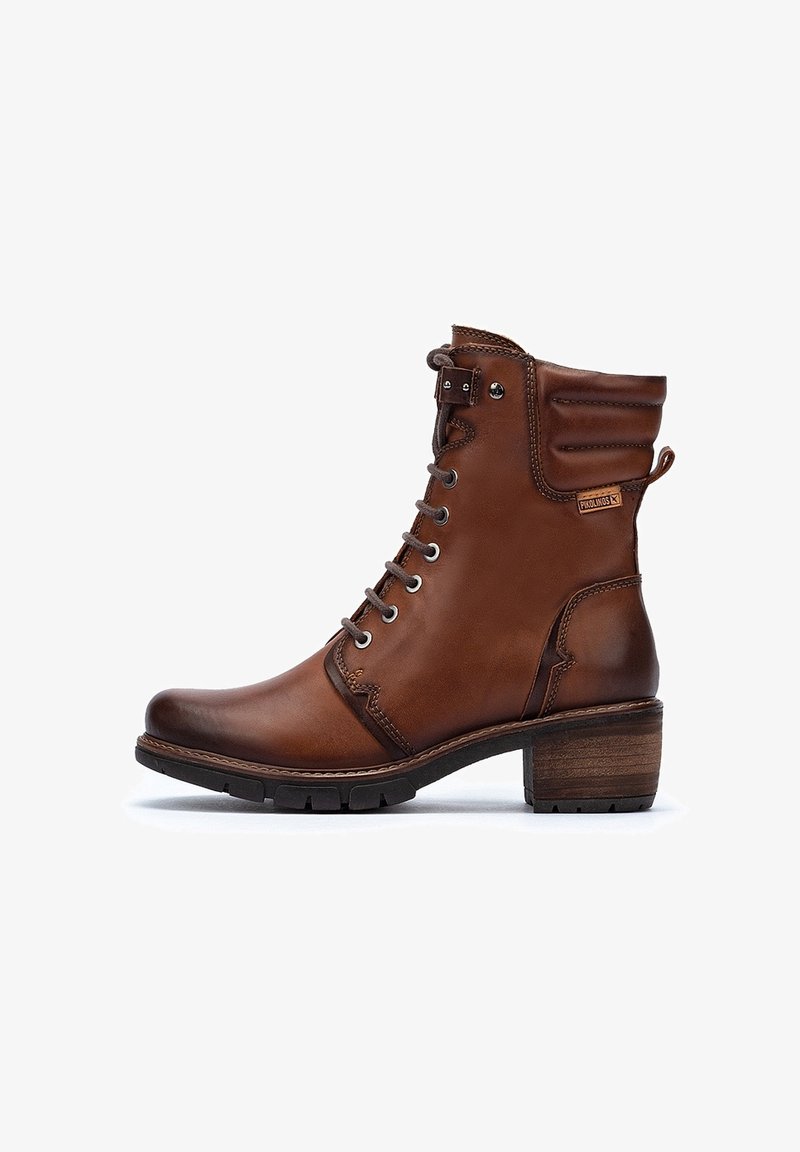 Stivaletto in pelle marrone con punta rotonda, laccato sul fronte, collo imbottito e un tacco in legno spesso. Dettagli testurizzati sui lati.
