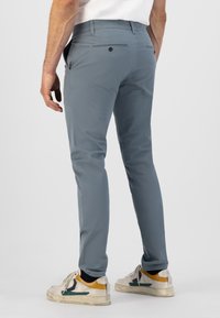 Pantalons slim gris à texture lisse, avec des poches arrière et un détail de bouton unique, associés à des baskets blanches et jaunes.