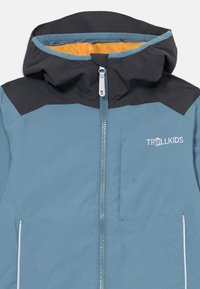 Niebieska i czarna kurtka z kapturem, z zamkiem z przodu, pomarańczową podszewką i logo "TROLLKIDS" na klatce piersiowej. Gładka tekstura, sportowy design.