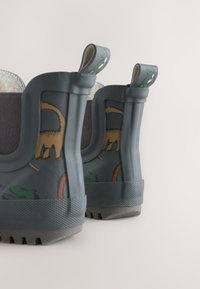 Bottes en caoutchouc grises avec des détails texturés, ornées de motifs animaliers verts et orange. Doublure intérieure douce ; languettes à l'arrière pour un enfilage facile.