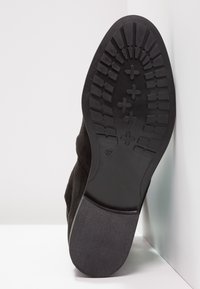 Suela de zapato negra con un patrón de profundidad, tamaño 37, exhibida en posición vertical contra un fondo blanco en la esquina.