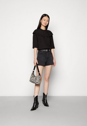 Blusa preta canelada com colarinho com babados, combinada com uns calções de ganga pretos. Botins de pele pretos até ao tornozelo e uma mala de zebra completam o visual.
