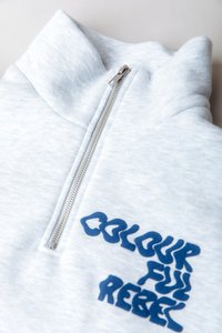 Sudadera de media cremallera en gris claro con cremallera plateada y texto estilizado azul "Colourful Rebel" en el pecho.