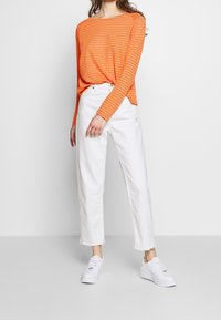 Orange och vit randig långärmad skjorta i kombination med högmidjade vita jeans och vita sneakers; avslappnad passform, minimalistisk design.