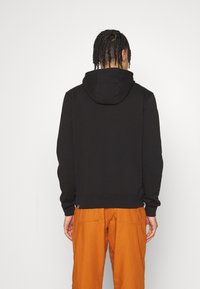 Černá mikina s kapucí, uvolněného střihu, s žebrovanými manžetami a spodním lemem. Nosit s oranžovými kalhotami volného střihu. Hladký materiál, minimální detaily.