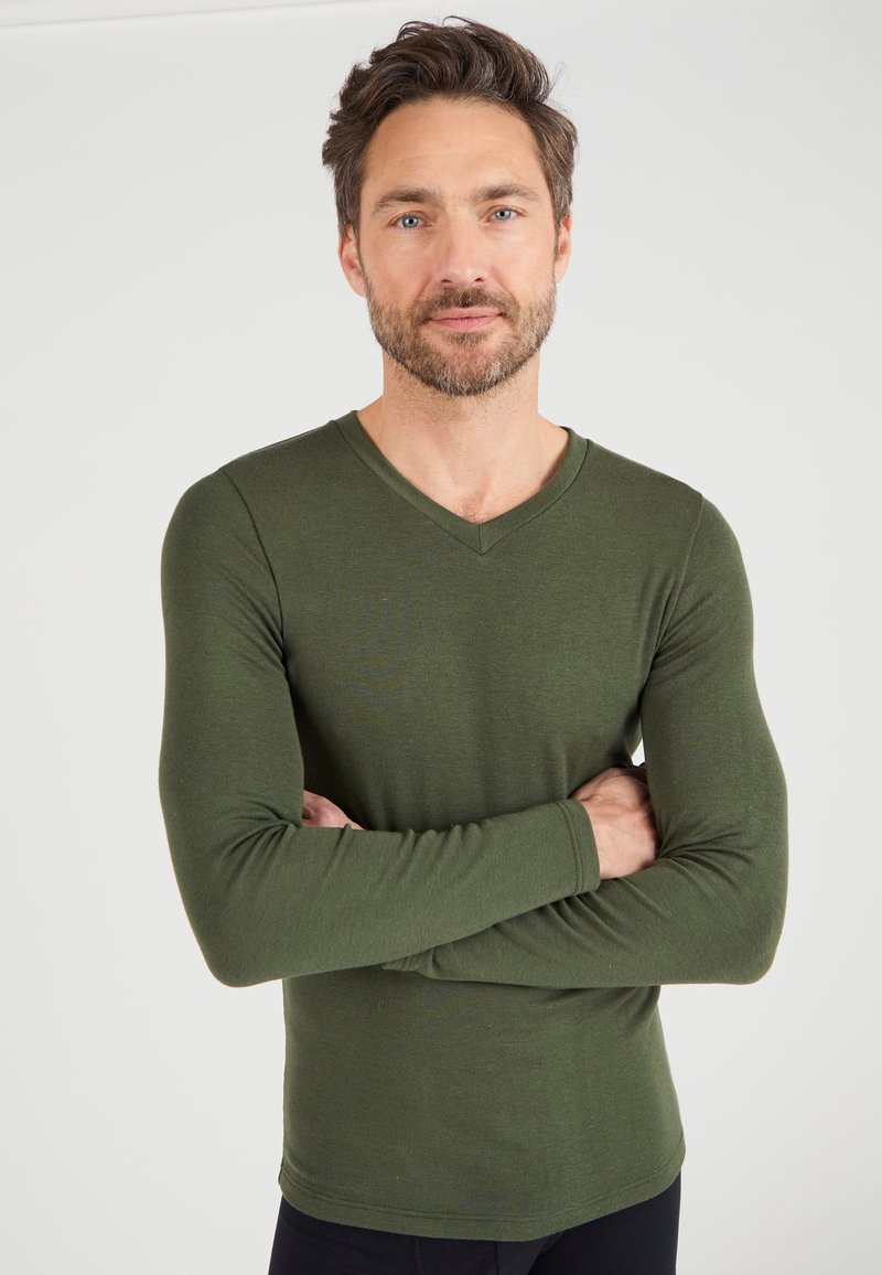 Olijfgroen langarm V-hals shirt van zachte stof, met een getailleerd ontwerp en een geribbelde manchet, gedragen door een man met gekruiste armen.