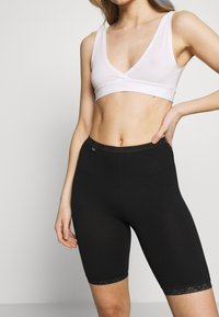 Zwarte elastische fietsshorts met een kantafwerking en een comfortabele tailleband, gecombineerd met een witte, mouwloze bralette met een V-hals ontwerp.