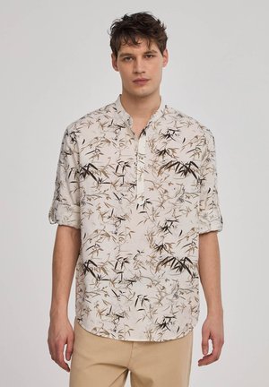 Camicia a maniche corte di colore chiaro con motivo a foglie in verde e marrone. Presenta una chiusura senza bottoni e una vestibilità comoda.