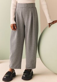 Pantalones de talle alto con estampado de pata de gallo en blanco y negro, con pliegues y diseño de pierna ancha, combinados con mocasines de plataforma negros.