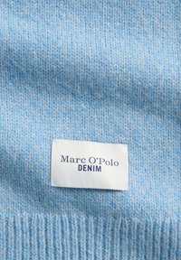 Jasnoniebieska dzianina o miękkiej fakturze, z białą metką z napisem "Marc O'Polo" i "DENIM" w granatowym kolorze.