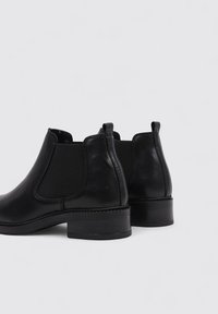 Botines de cuero negro hasta el tobillo con paneles laterales de elastano y un tacón bajo tipo bloque. Acabado suave con costuras decorativas y lengüetas en la parte posterior.