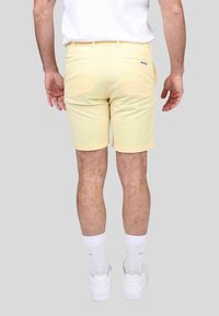 Shorts en coton jaunes au design slim, avec deux poches arrière et un détail de logo discret. Associés à des baskets blanches et des chaussettes.