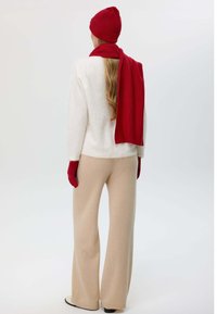 White, textured sweater with cream wide-leg pants, red ribbed knit hat, scarf, and gloves. Overall soft, cozy winter outfit with a warm color palette.