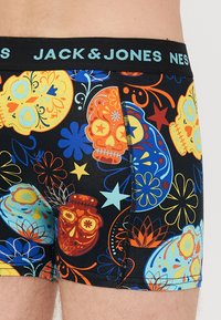 Svart boxer shorts med fargerike hodeskalle- og blomsterdesign. Elastisk midjebånd med "JACK & JONES" logo i lyseblått. Myk stofftekstur.
