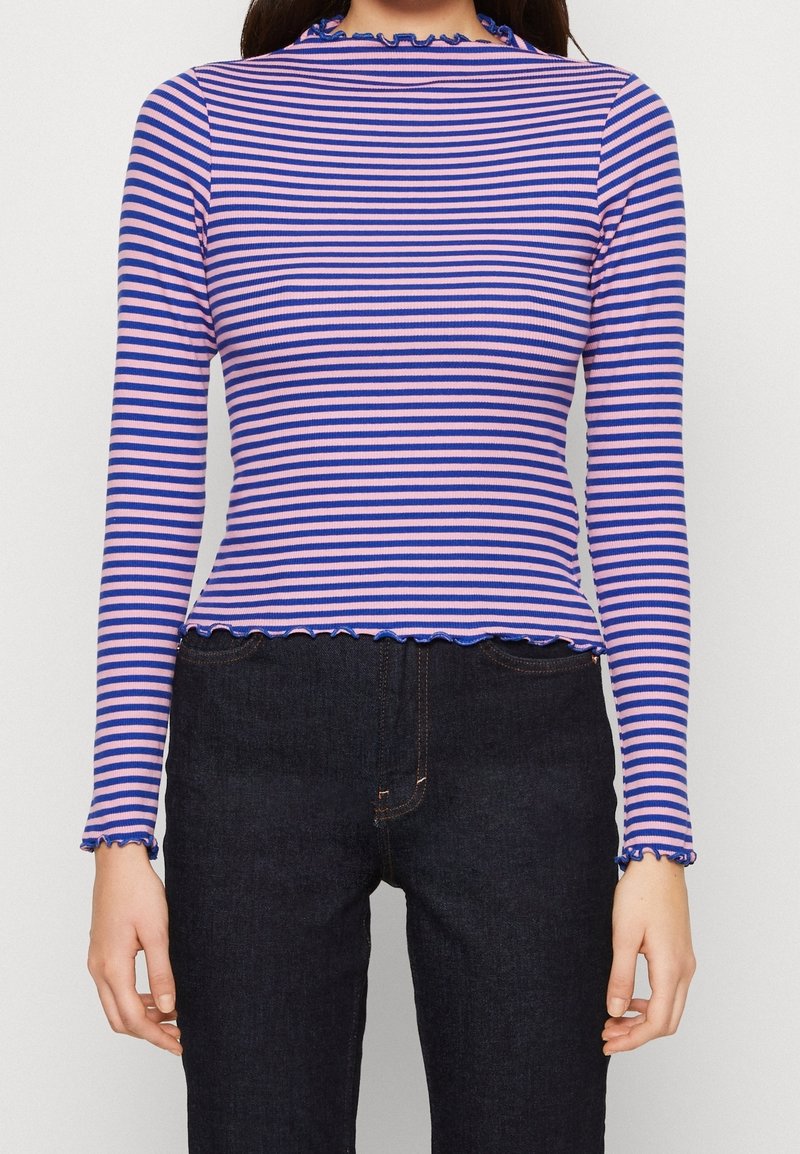 Paski długi rękaw w kolorach różowym i niebieskim z prążkowaną fakturą. Posiada falbaniaste wykończenie dekoltu i dołu, zestawiony z ciemnymi dżinsami.