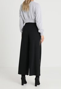 Maglione corto grigio melange con pantaloni neri a gamba larga a coste, caratterizzati da spacchi laterali. L'outfit è completato da stivali neri con tacco alto.