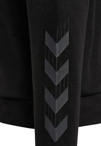 Svart sweatshirt med texturerad tyg, med ett glänsande chevronmönster längs ärmen i mörkgrått. Minimalistisk design.