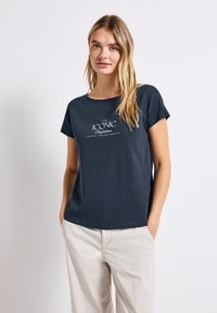 T-shirt à manches courtes bleu marine foncé en coton doux, avec un design de texte blanc qui dit "CONFIANCE ICONIQUE" centré à l'avant.