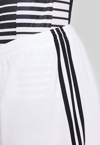 Pantalones cortos deportivos blancos con rayas negras a los lados, fabricados con un tejido ligero. Cuentan con una cinturilla elástica y una textura suave.