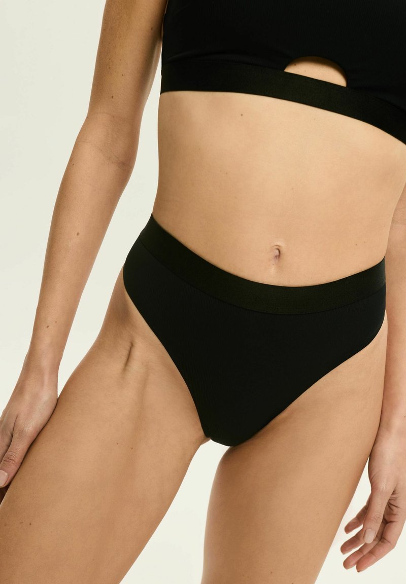 Czarne, prążkowane majtki bikini o wysokim kroju i szerokim pasie. Gładka tekstura, minimalne detale i elegancka sylwetka.