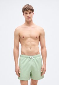 Πράσινα ριγέ μαγιό σορτς από ελαφρύ ύφασμα, με ελαστική μέση και κορδόνι ρύθμισης, σε άνετη γραμμή.