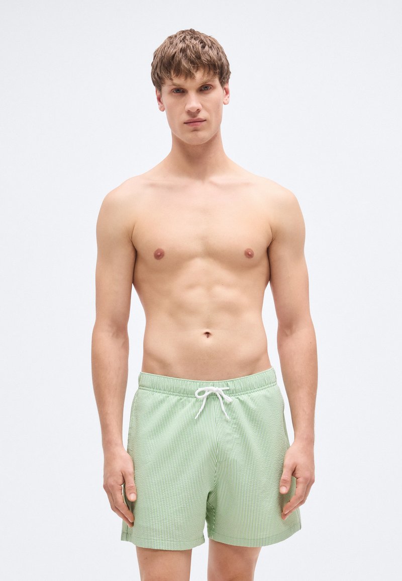 Πράσινα ριγέ μαγιό σορτς από ελαφρύ ύφασμα, με ελαστική μέση και κορδόνι ρύθμισης, σε άνετη γραμμή.