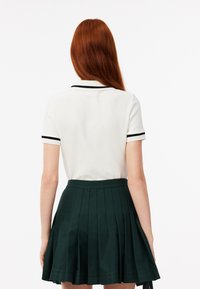 Witte polo met korte mouwen en zwarte accenten, gecombineerd met een donkergroen geplisseerde rok, die een gestructureerde stof en een aangesloten ontwerp toont.