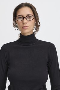 Le pull à col roulé noir présente une coupe ajustée. Accessoirisé de lunettes écaille de tortue et de boucles d'oreilles argentées audacieuses. Texture lisse.