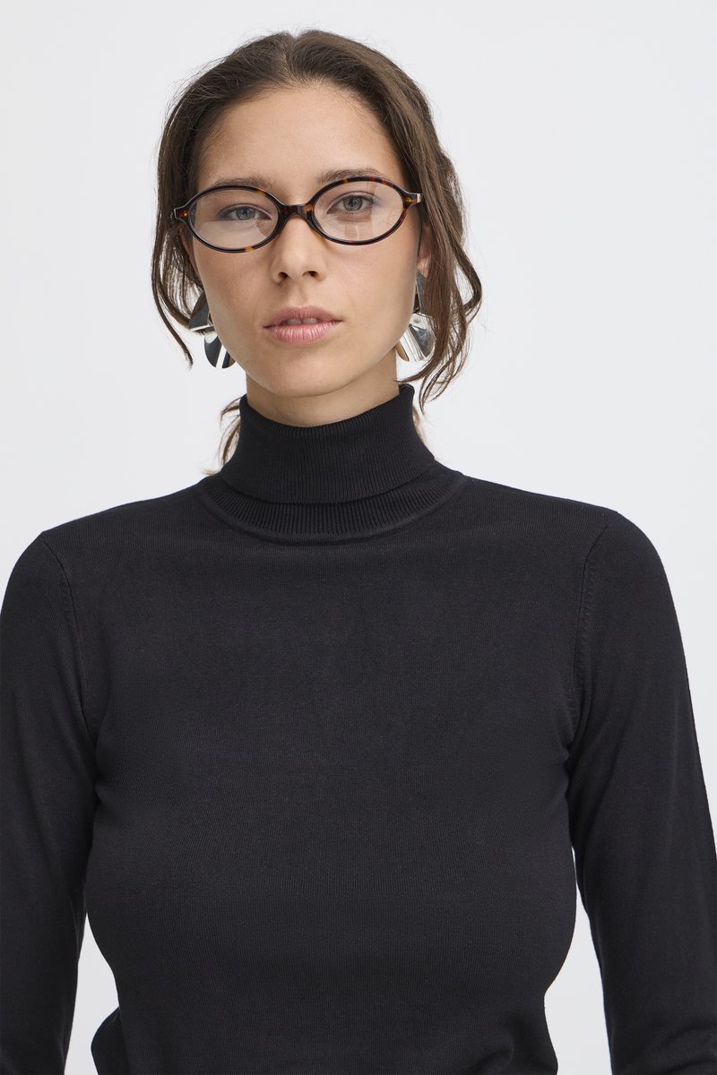 Le pull à col roulé noir présente une coupe ajustée. Accessoirisé de lunettes écaille de tortue et de boucles d'oreilles argentées audacieuses. Texture lisse.