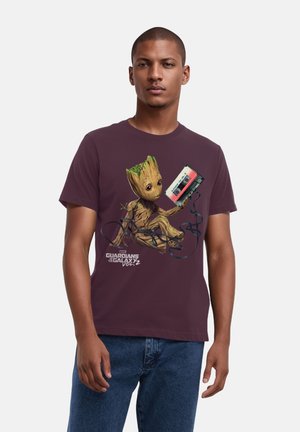 Maroon cotton t-shirt featuring a graphic of a character with wood-like texture and green accents, holding a cassette tape with black cord.