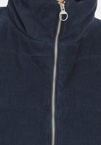 Manchesterjacka i mörk marinblå med hög krage, vertikal textur och en silverfärgad dragkedja framtill, med en ren, strukturerad design.