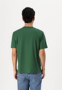 Κοντομάνικη πράσινη μπλούζα από βαμβάκι, με στρογγυλή λαιμόκοψη και χαλαρή εφαρμογή, με λεία υφή και χωρίς ορατά σχέδια.