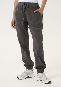 Grå, lätta joggerbyxor med elastisk midja och dragsko, med sidofickor och elastiska muddarna. Bärs med vita sneakers.