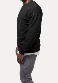 Felpa nera con collo tondo e maniche lunghe, realizzata in tessuto morbido. Abbinata a jeans grigi con pannelli laterali testurizzati.