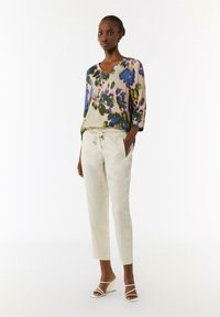 Bluse mit Blumenmuster aus weichem Stoff, mit V-Ausschnitt und Dreiviertelärmeln, kombiniert mit hellbeigen Pull-on-Hosen und Wedgesandalen.