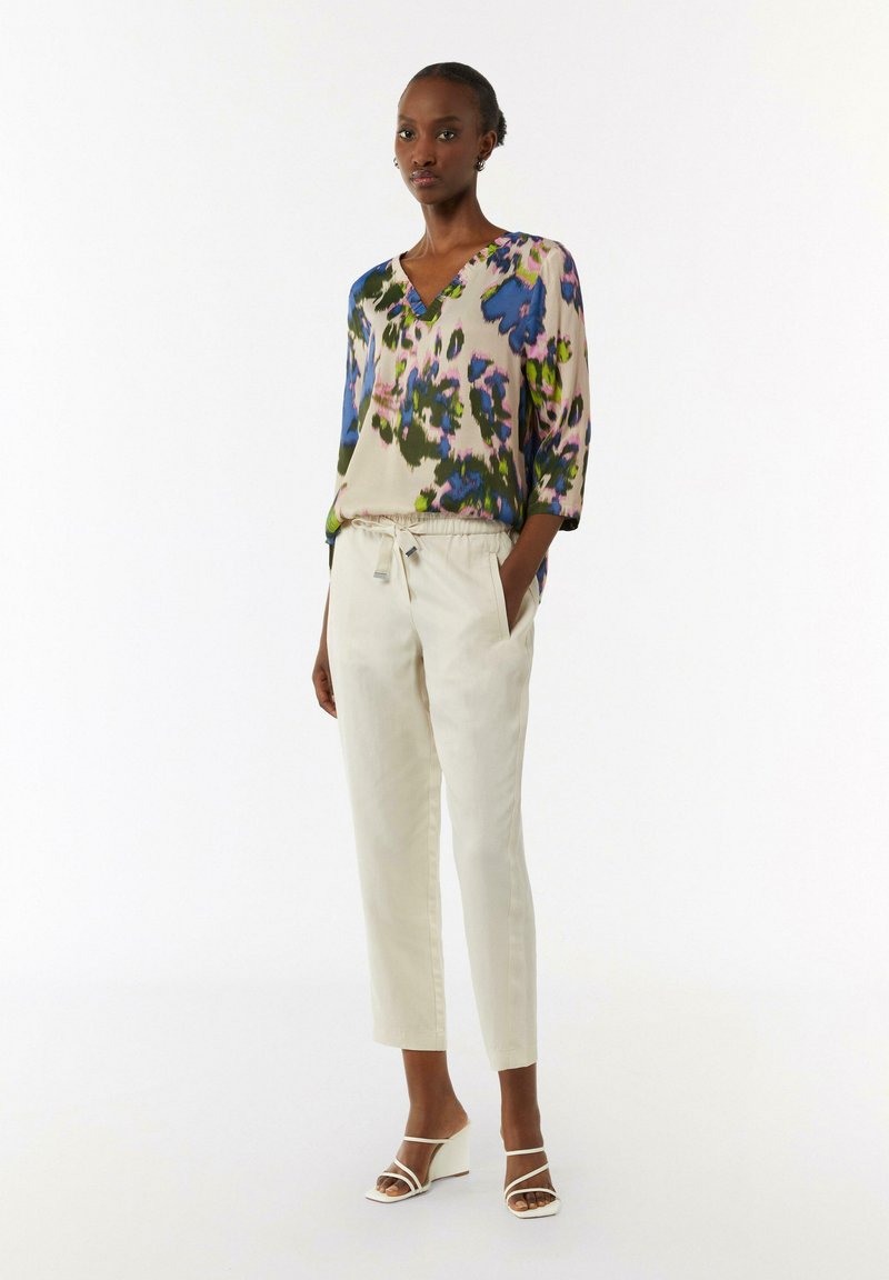 Bluse mit Blumenmuster aus weichem Stoff, mit V-Ausschnitt und Dreiviertelärmeln, kombiniert mit hellbeigen Pull-on-Hosen und Wedgesandalen.