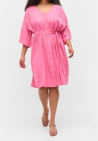 Różowa sukienka z paskiem, z dekoltem w serek, podwiniętymi rękawami i bocznymi rozcięciami, wykonana z gładkiego materiału o luźnym kroju.