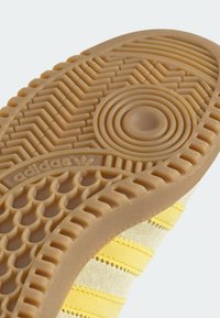 Kumirubber-pohja, jossa on sahalaitakuvioita ja ympyräkuvioita, sekä teksturoitu pinta. Yläosa keltaista, jossa vaaka-alueita ja mokkanahkaa.