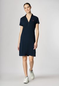 Abito navy a maniche corte con colletto e zip frontale, caratterizzato da un piccolo logo ricamato sul petto. Tessuto in cotone liscio, lunghezza ginocchio.