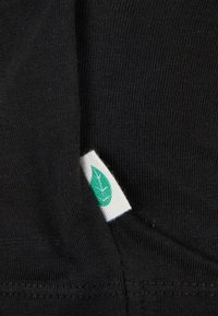 Tissu noir avec une petite étiquette blanche portant un symbole de feuille verte cousue dans la couture, indiquant un matériau écologique.
