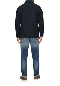 Marineblaues Wollmischgewebe-Jackett mit Kragen, geknöpften Bündchen und Yoke-Detail im Rücken, getragen über hellblauen, verwaschenen Jeans und Sneakers.