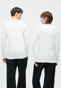 Valget värvitud pika varrukaga ümara kaelusega särk, millel on sile pind ja istuv lõige. Nähtavad õmblused rõhutavad struktuuri. Kandmiseks mustad püksid.