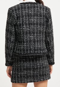 Czarny i biały żakiet w kratę o teksturowanym wykończeniu oraz pudełkowym kroju, z charakterystycznym wzorem i dopasowanymi rękawami.