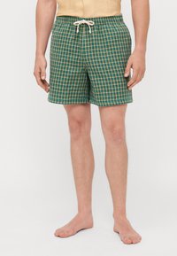 Costume da bagno verde a quadretti con cintura regolabile. Il motivo presenta dettagli gialli e il tessuto sembra testurizzato.